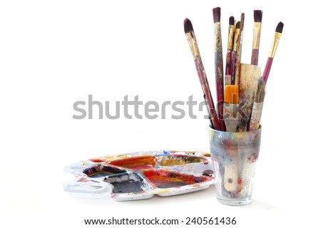 bunch of paint brushes in a glass and a used palette with colors, isolated on white background