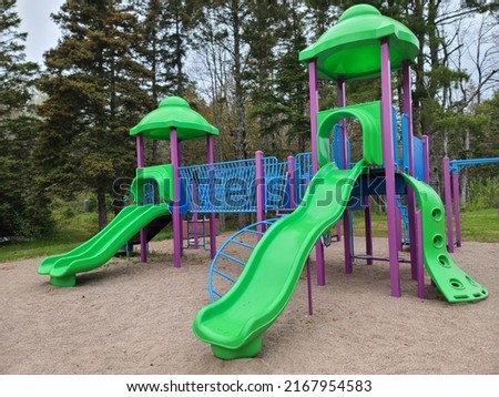 A bunch of playground equipment at a park. The metal and plastic jungle gym are bright shades of green, blue, and purple.