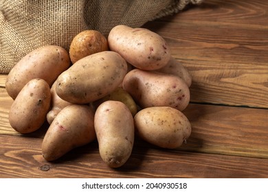 Bunch Of Potatoes After Harvest Lying On Wooden Boards With A Potato Sack In The Background