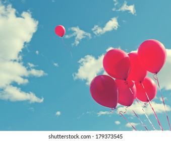 Bunch of red balloons on a blue sky with one balloon escaping to be individual and free - concept for following one's dreams