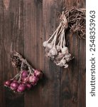 A bunch of red onions and a bunch of garlic hanging against a wooden backdrop