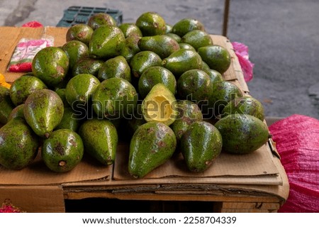 Bunch of Ripe Avocados on a Carboard Sheet on a Stall in Colorful Market 