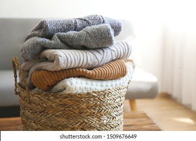 Bunch Of Stacked Knitted Pastel Color Sweaters With Different Knitting Patterns Perfectly Folded In Wicker Basket On Table, Living Room Background. Fall Winter Season Knitwear. Close Up, Copy Space.