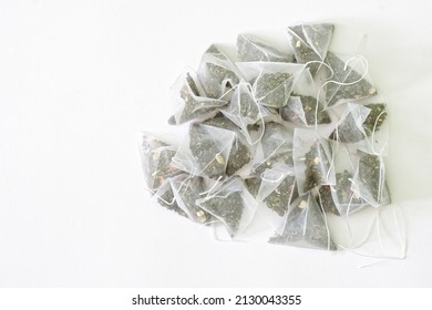 Bunch of tea bags-pyramids with green tea with the addition of fragrant fruits. Textured white background. Copy space for an inscription. Daylight - Shutterstock ID 2130043355