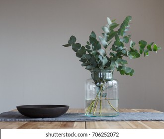 A Bunch Of Twigs And Green Eucalyptus In A Glass Jar On The Wooden Table.