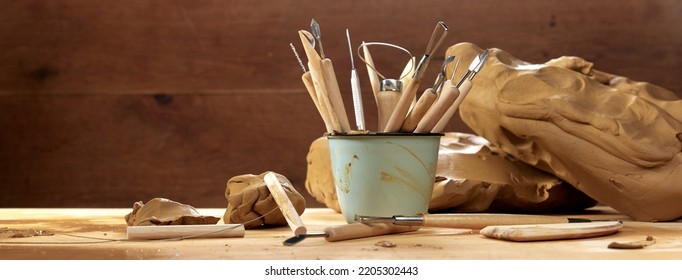 Bunch of various instruments for sculpting pottery in metal mug placed on wooden table with clay in professional light workshop