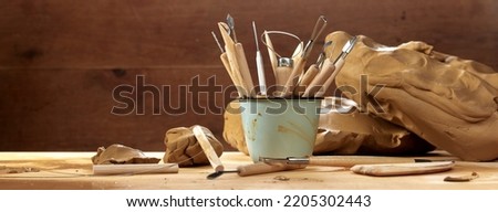 Bunch of various instruments for sculpting pottery in metal mug placed on wooden table with clay in professional light workshop