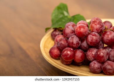 Bunches of fresh ripe red grapes on wooden dish and floor with branch , red wine grapes