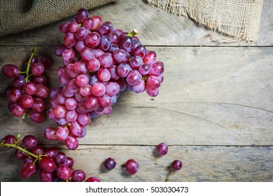 Bunches of fresh ripe red grapes on a wooden textural surface. Ancient style, a beautiful background with a branch of blue grapes. Red wine grapes. dark grapes, blue grapes, wine grapes