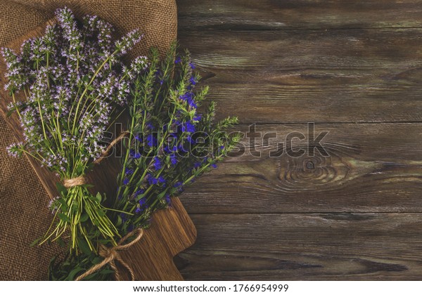 Bunches of\
medicinal herbs with purple and blue flowers copy space. Thyme and\
hyssop flowers on a wooden table flat\
lay.