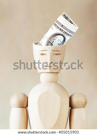 Bundle of dollars into the human head. Abstract image with wooden puppet