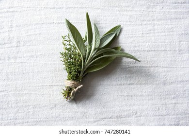 Bundle Of Fresh Green Aromatic Herbs Thyme, Rosemary And Sage, Tied With A Thread To Be Used In Cooking. Close Up Photo On A White Cloth.