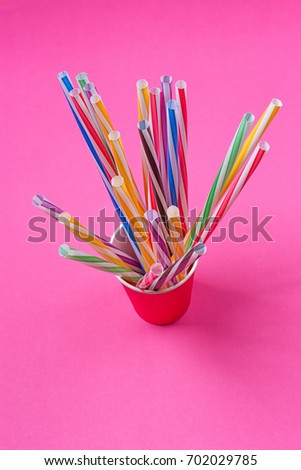 a bundle of multi-colored drinking straws in a paper Cup on a pink background. fashion minimal. flat lay