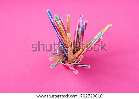 a bundle of multi-colored drinking straws in a paper Cup on a pink background. fashion minimal. flat lay