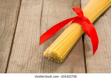 Bundle of raw spaghetti tied with red ribbon on wooden surface - Powered by Shutterstock