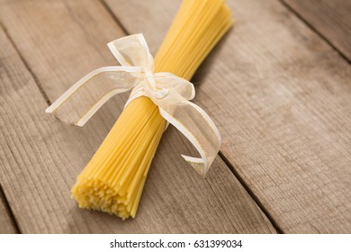 Bundle of raw spaghetti tied with white ribbon on wooden surface - Powered by Shutterstock