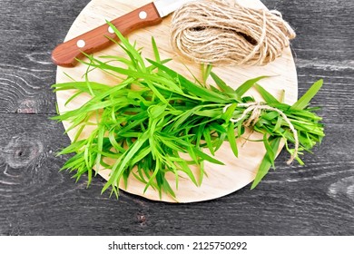 A bundle of tarragon tied with twine, a coil of rope and a knife on a background of a wooden board from above