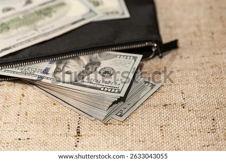 Bundle of US dollar bills in closed black wallet on textile surface, concept of savings, personal budget and secure money storage

