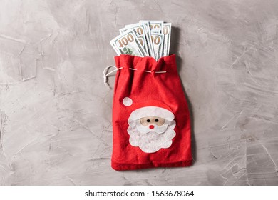 Bundle Of US Hundred Dollars In The Funny Santa Claus Red Bag From Felt On The Gray Concrete Background. Cristmas Concept. 