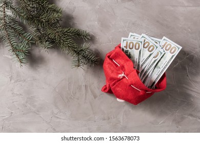 Bundle Of US Hundred Dollars In The Funny Santa Claus Red Bag From Felt On The Gray Concrete Background. Cristmas Concept.  