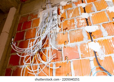 Bundle Of Various Cables Hang From A Plastic Fuse Box Mounted On The Wall, Building Under Construction, Work In Progress. Installation Of Electrical Wires And Cables.
