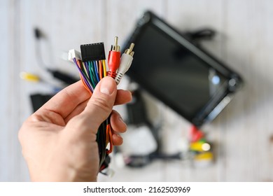 A Bundle Of Wires With Various Connectors In Hand Against The Background Of A New Car Radio. Selective Focus On Hand With Wires