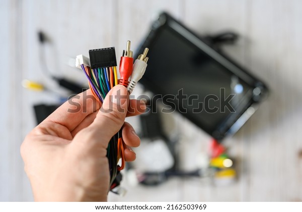 A bundle of wires with various connectors in hand\
against the background of a new car radio. Selective focus on hand\
with wires