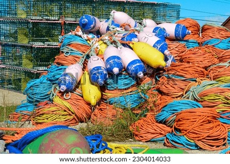 Bundles of commercial nylon woven fishing line orange, yellow, blue, and green in color. There are multiple buoys piled on top of the rope. The fishing gear is in a pile on a concrete platform. 