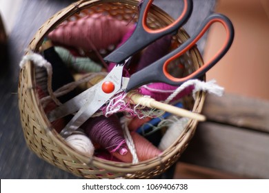 Bundles of thread in the basket, scissors and thread in drums on the table close up