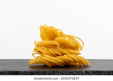 Bundles of uncooked spaghetti are artistically arranged on a textured black slate surface, lightly dusted with flour, creating a rustic culinary scene. - Powered by Shutterstock