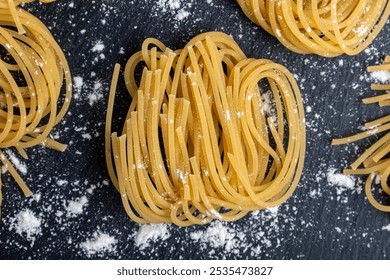 Bundles of uncooked spaghetti are artistically arranged on a textured black slate surface, lightly dusted with flour, creating a rustic culinary scene. - Powered by Shutterstock