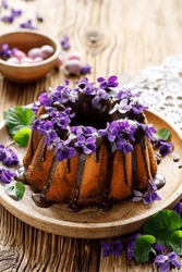 Bundt Cake With Chocolate Icing Decorated With Fresh Violets Flowers. Dessert With Edible Flowers