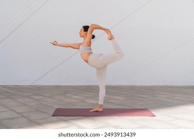 A bunette woman in sportswear doing the Natarajasana pose or dancer's pose with the background of modern buildings - Powered by Shutterstock