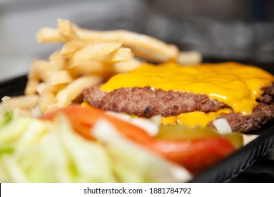 Bunless Triple Burger Meat Patties With Cheese Next To Shredded Lettuce, Sliced Tomatoes, Pickle Chips, And French Fries