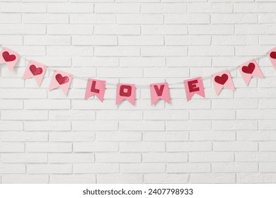 Bunting with word LOVE hanging on white brick wall. Valentine's Day celebration
