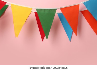 Buntings with colorful triangular flags hanging on pink background. Festive decor