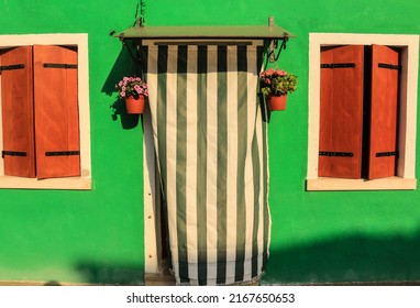 Burano, Venice, Italy - May 2022 : A Traditional Fisherman Green Color House With Brown Shutters And A Stripped Curtain On The Door.