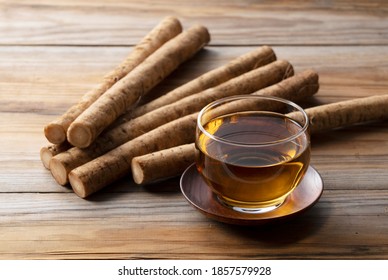 Burdock tea placed against a background of wooden boards. A raw burdock behind it