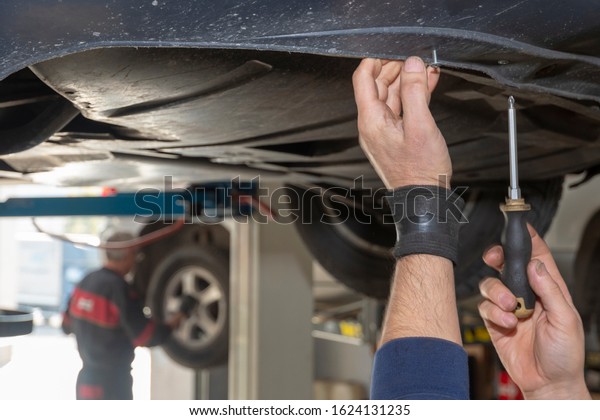 Burgas, Bulgaria - 11/12/19: Close up of the\
hands of a man using a screwdriver to disassamble the plastic cover\
on a customers car in the local automobile workshop. Repair service\
operation.