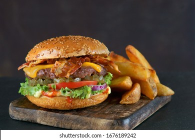 Burger with bacon, cheese and fried potatoes on a dark background