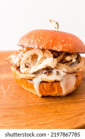 Burger With Beef Cutlet Under Tender Cream Cheese With Champignons And Onion Chips On A Wooden Plate On A White Background. Vertical Photo