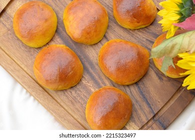 Burger buns on wooden board. Home baked pumpkin bread rolls with gold crust and fluffy crumb. Pumpkin buns with yellow coloured crumb for delicious burger sandwich with sunflower bouquet in background - Shutterstock ID 2215323497