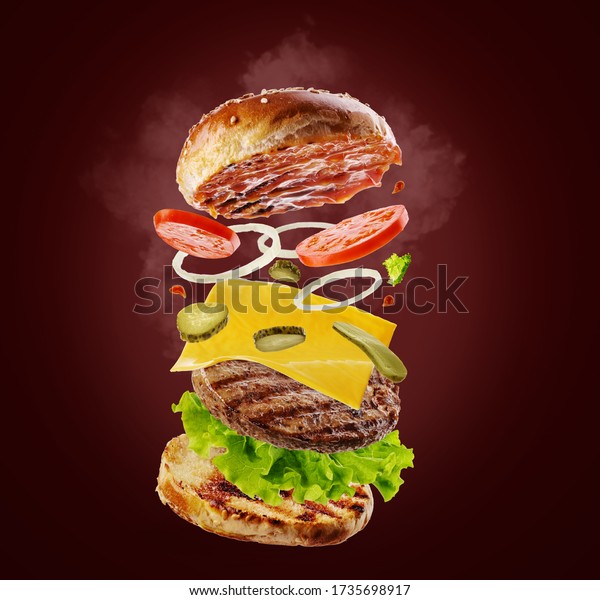 Burger with flying elements. Delicious hamburger\
with flying ingredients isolated on red background.  Food\
levitation concept.