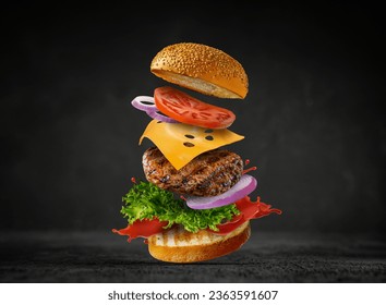 Burger with flying elements. Delicious burger with flying ingredients isolated on black background. Flying Burger Slices - Powered by Shutterstock