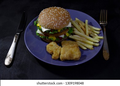 burger, french fries and nuggets on blue ratel on black wooden background