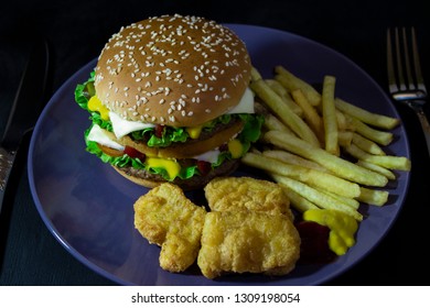 burger, french fries and nuggets on blue ratel on black wooden background