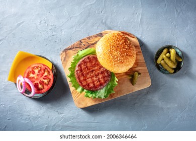 Burger Ingredients. Hamburger Beef Patty, Green Salad Leaf, Cheddar Cheese, Tomato And Red Onion, With Pickles, Overhead Shot On A Blue Background