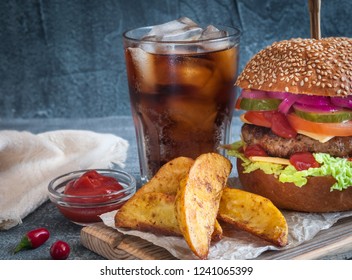 Burger with juicy cutlet and vegetables. Spicy sauce and carrots in country style. A glass of cola with ice. On a dark background a blurred background.