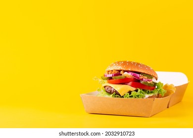 Burger With A Marble Beef Patty In Open Paper Package On A Yellow Background. Space For Text.