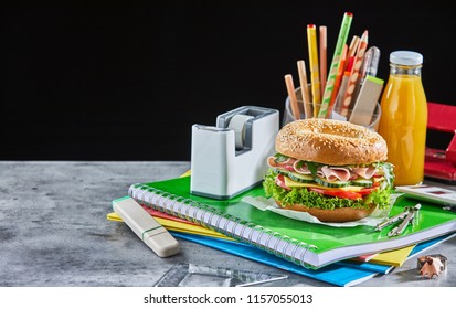 Burger And Orange Juice Bottle On School Supplies Next To Clear Pencil Holder And White Rectangular On Marble Table With Black Background Tape Dispenser